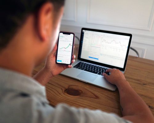 image of man at desk trading on laptop and phone